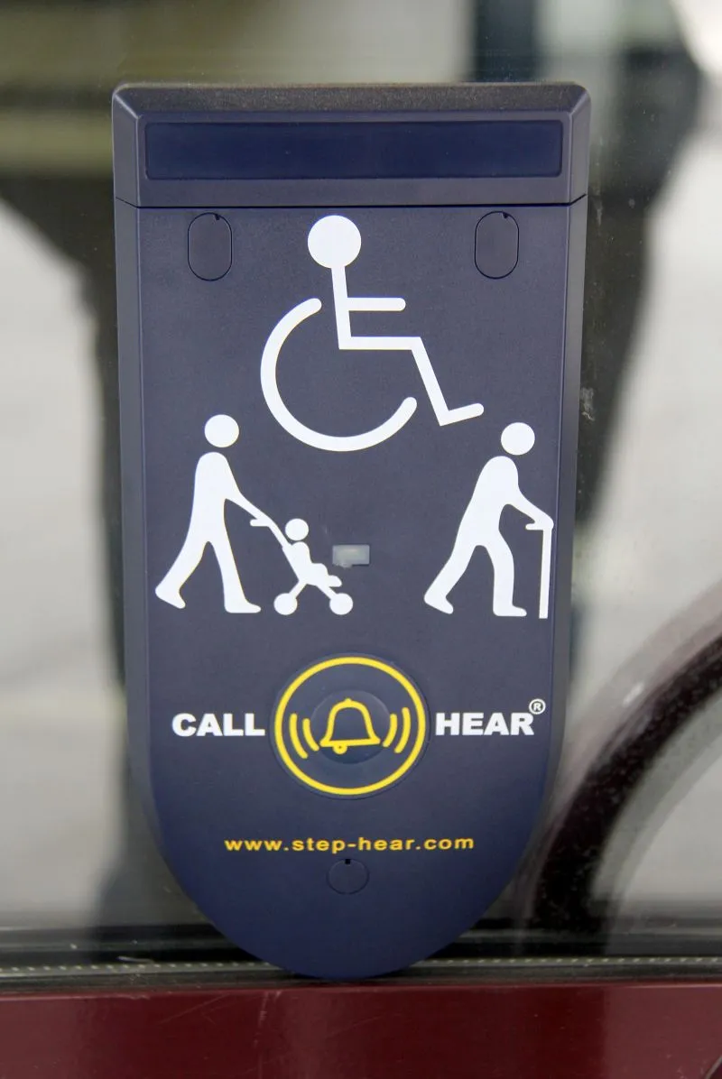 Panel z ikonami osoby na wózku inwalidzkim, osoby z wózkiem dziecięcym oraz osoby z laską, wraz z napisem "CALL HEAR" i symbolem dzwonka.